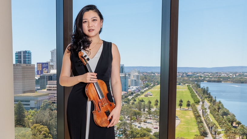Emily Sun wearing a black evening dress posing with "The Adelaide" violin.
