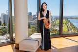 Emily Sun wearing a black evening dress posing with "The Adelaide" violin.