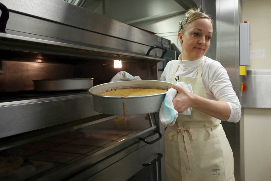 A baker takes a cake out of an oven.