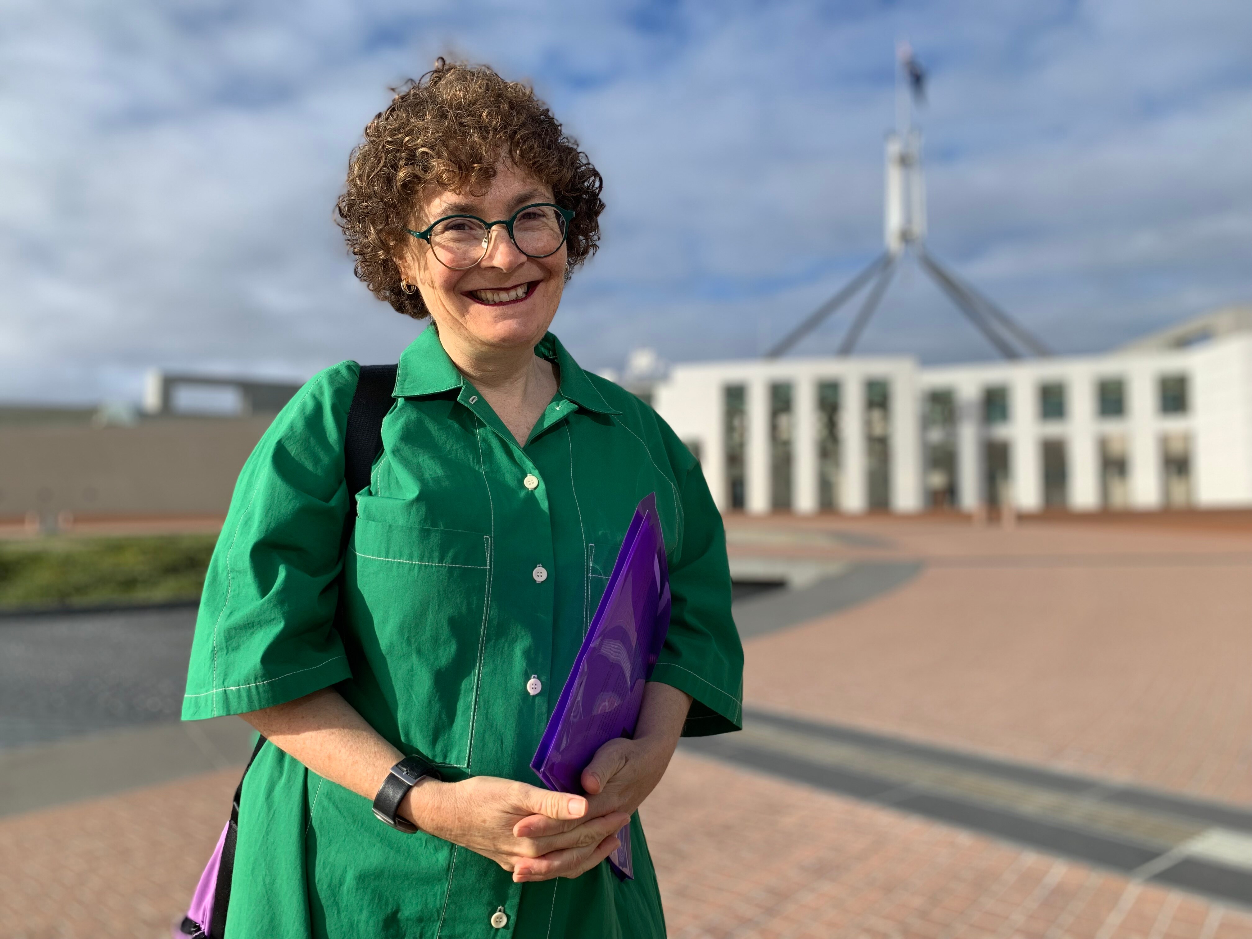 A middle aged woman with short curly hair and glasses standing out the front of Parliament House in Canberra