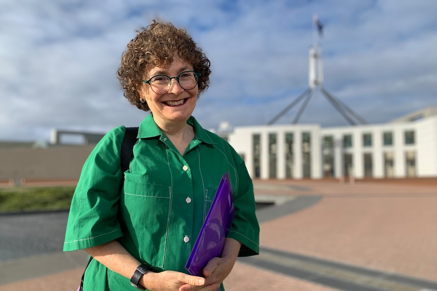 A middle aged woman with short curly hair and glasses standing out the front of Parliament House in Canberra