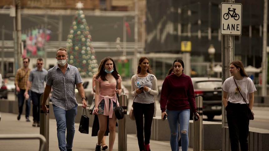 People walk across a bridge, with a Christmas tree in the background.