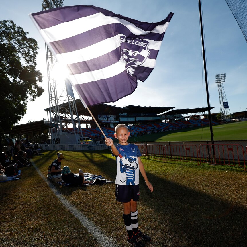 A young Geelong fan holds a large Cats flag at Marrara Oval