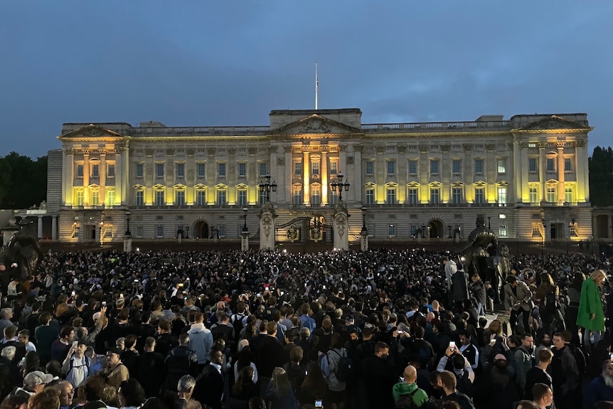 A large crowd of people outside Buckingham Palace at night