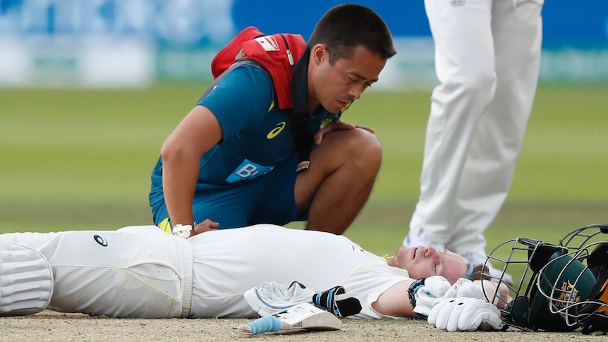 Steve Smith lies on his back with his arms splayed out alongside him as a physio kneels over him