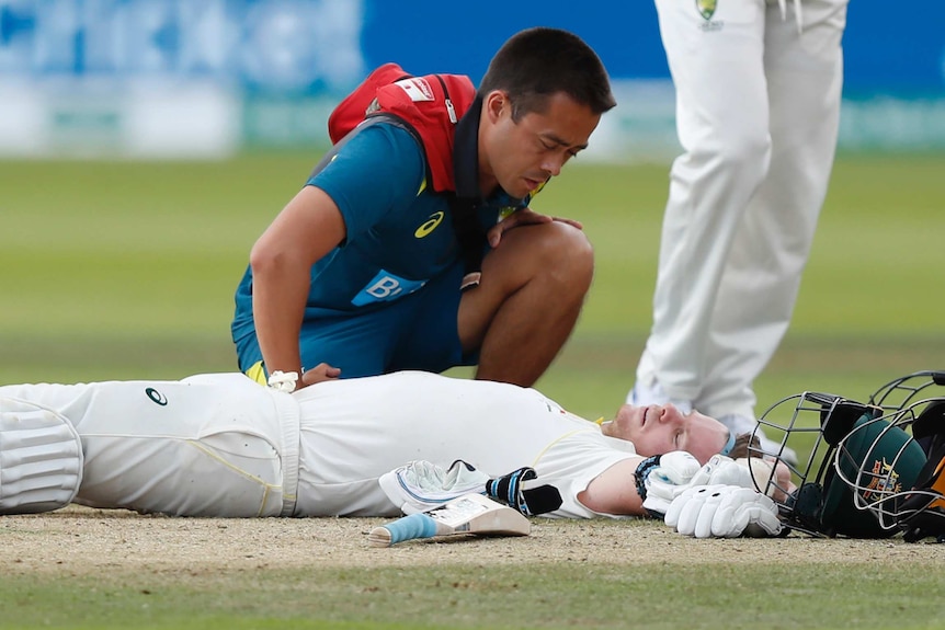 Steve Smith lies on his back with his arms splayed out alongside him as a physio kneels over him