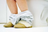 A woman's feet as she sits on the toilet.
