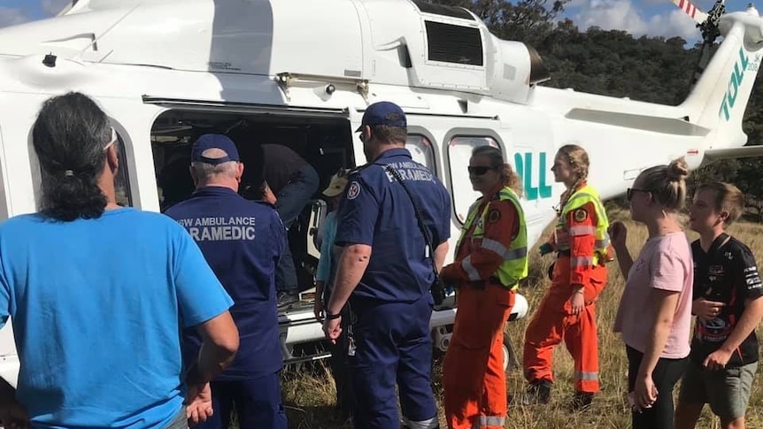 SES volunteers, NSW paramedics and civilians in front of a helicopter in a field.