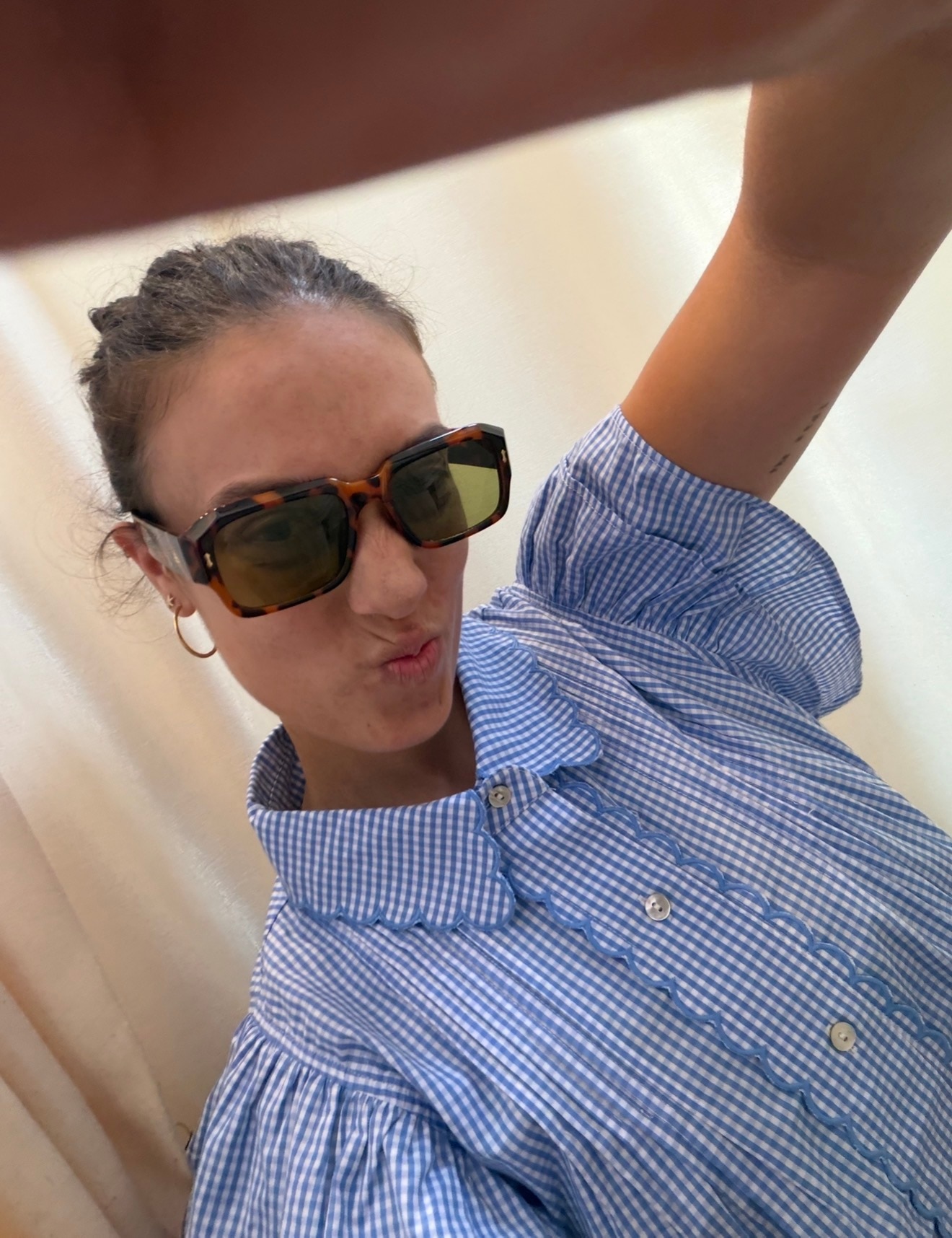 Mikaela posa con gafas de sol y una camisa azul con botones a cuadros.