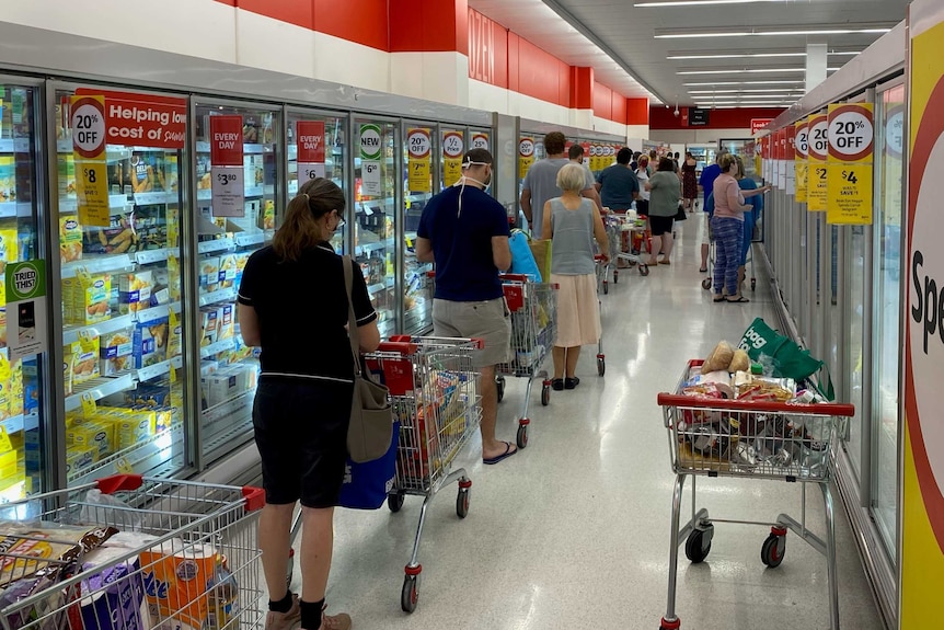 A long line of shoppers with trollies lining up in the frozen food section of a Coles store.