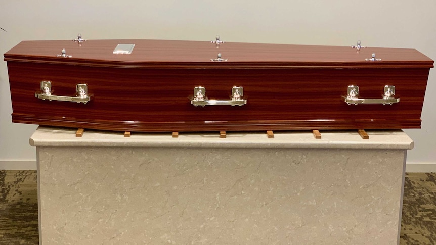 A brown wood coffin sits on a bench in a funeral parlour.