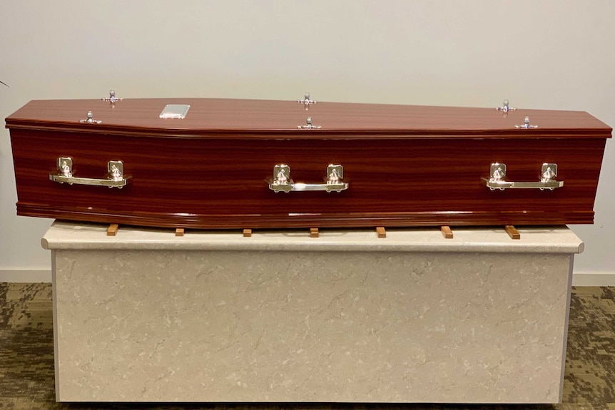 A brown wood coffin sits on a bench in a funeral parlour.