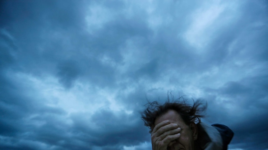 Man covers his eyes from a gust of wind and a blast of sand as Hurricane Florence approaches.