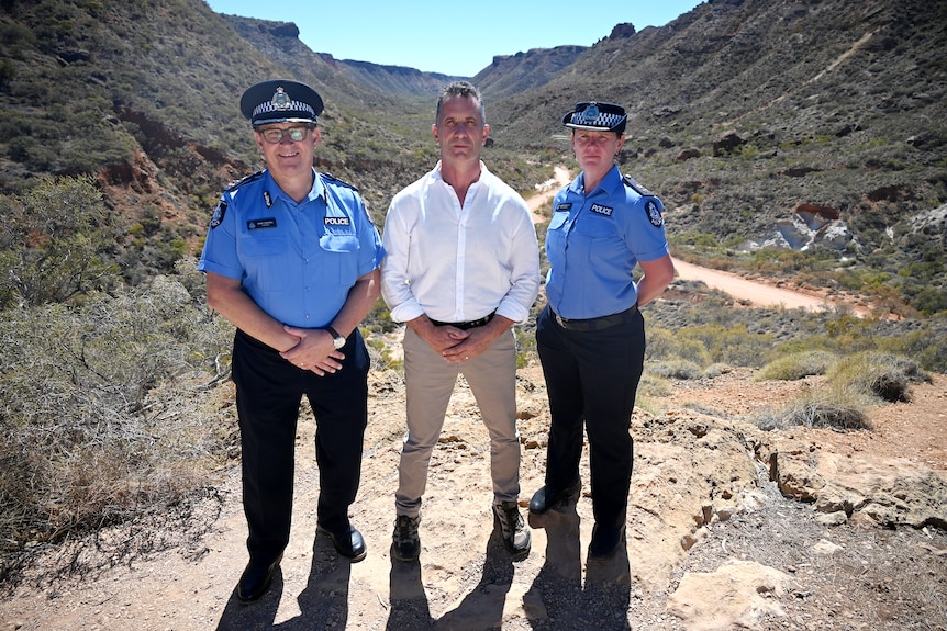 Tow police officers, a man and woman, and a second man in a white shirt stand on a rocky surface with a canyon vista behind