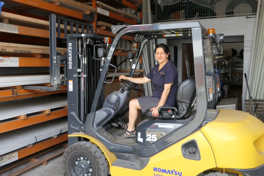A woman operates a forklift in a storeroom.