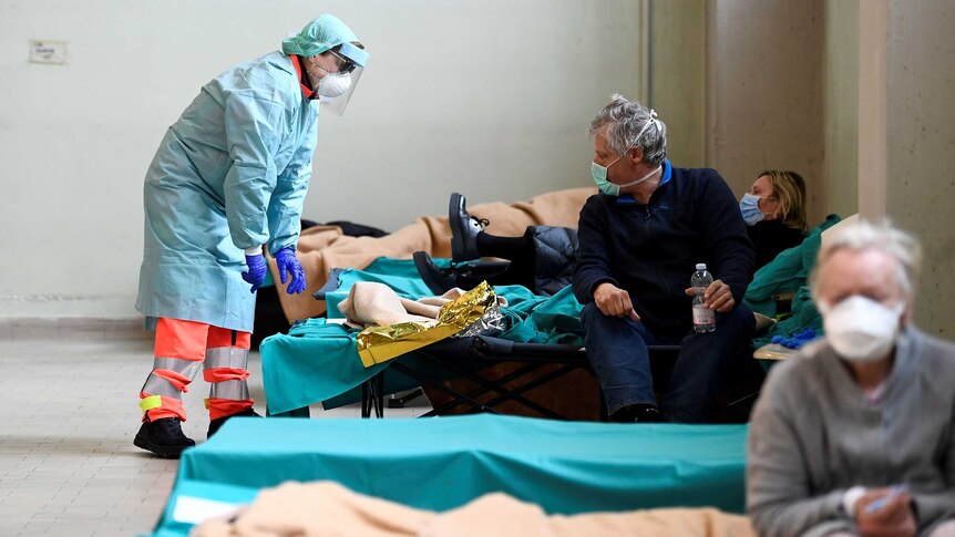 A female health worker in full hazmat gear leans over a man's bed