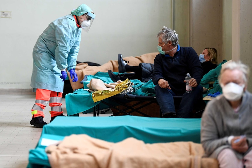 A female health worker in full hazmat gear leans over a man's bed