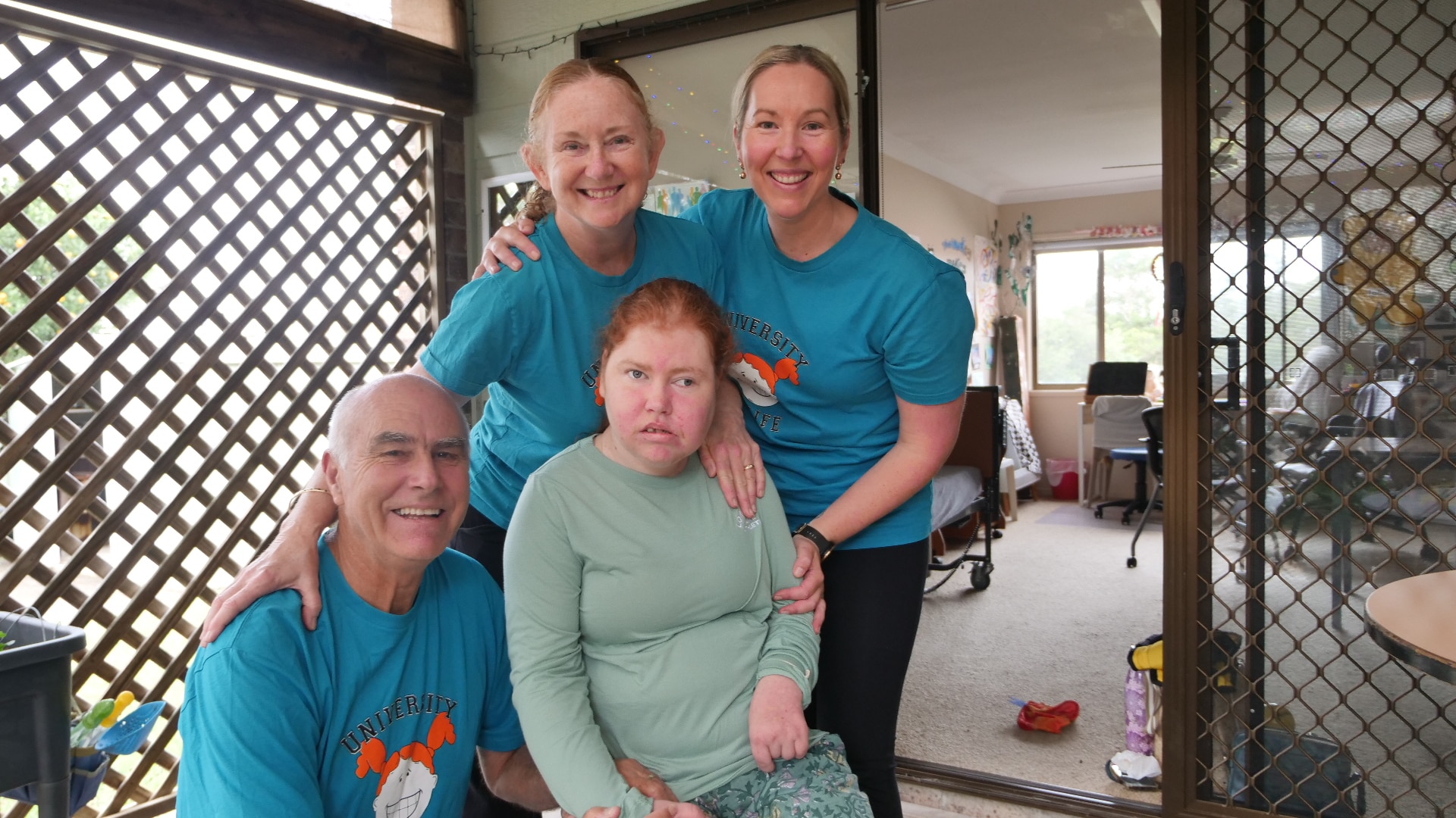 A family portrait with father, mother and support worker in blue T-shirts behind Lillian sitting in front of her learning room