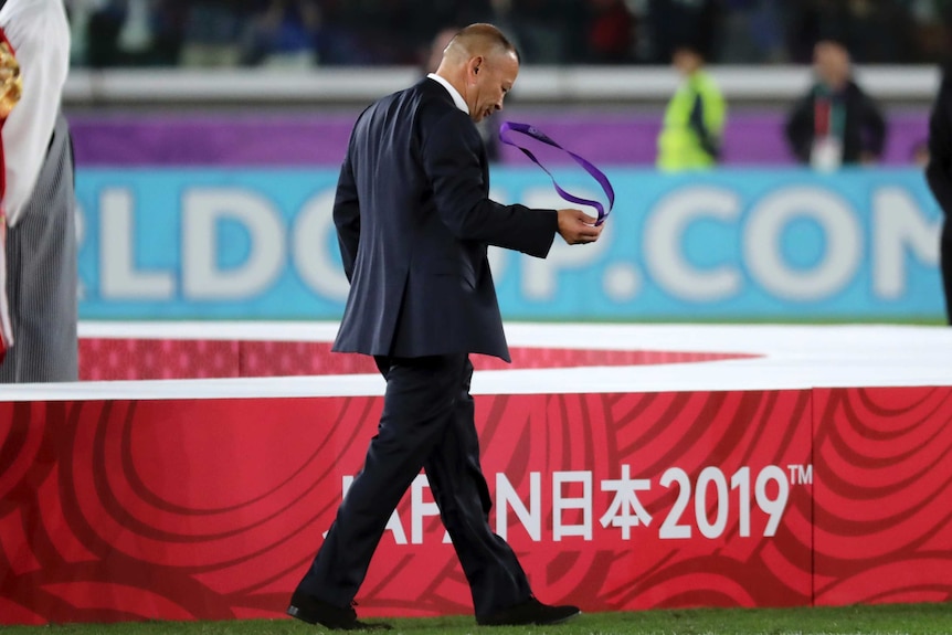 Eddie Jones, wearing a suit, takes a medal from around his neck and walks away