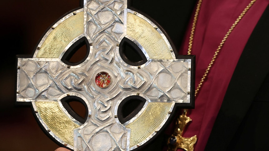 A silver cross with a red centre is held by a person out of frame.