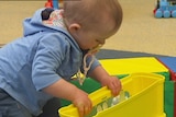 Video still: Good generic photo of a young toddler playing with a bright yellow toy at child care. Aug 2012