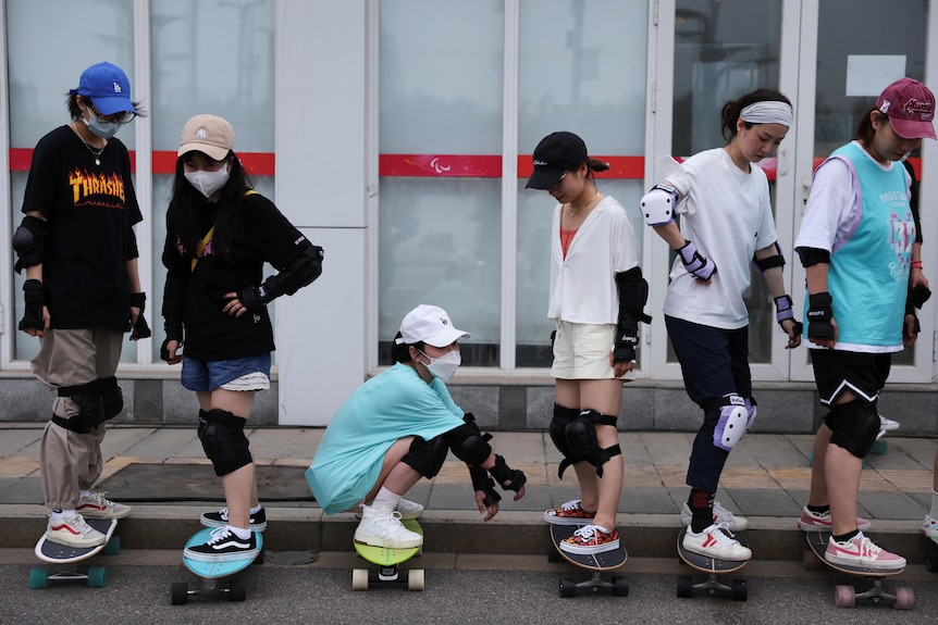 Six women on sakeboards on the edge of a street. 