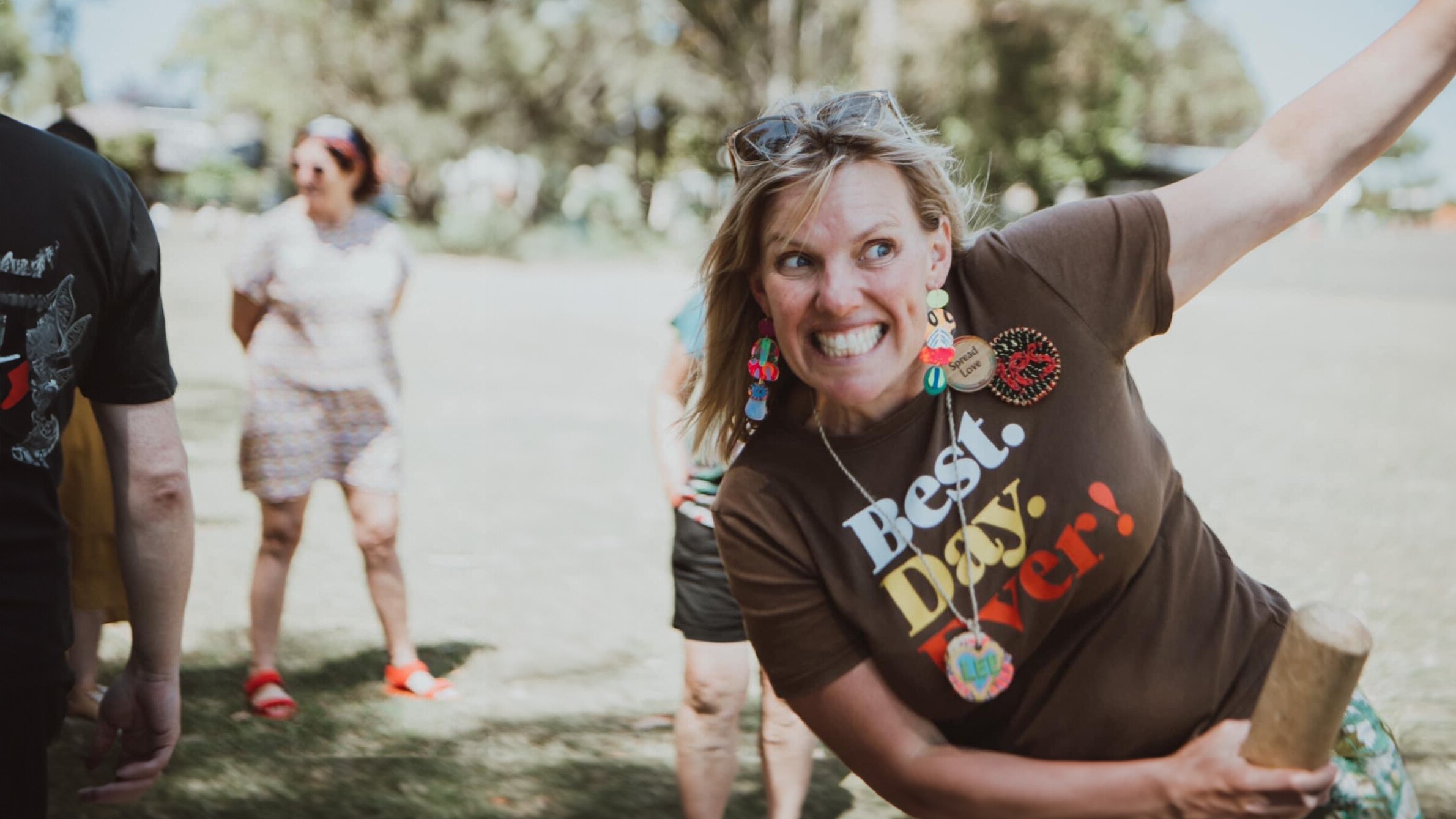A woman with a glowing smile is playing a game outdoors with friends.