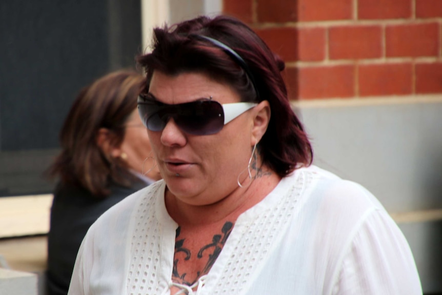 A woman with brown hair and wearing sunglasses and a white top outside court.