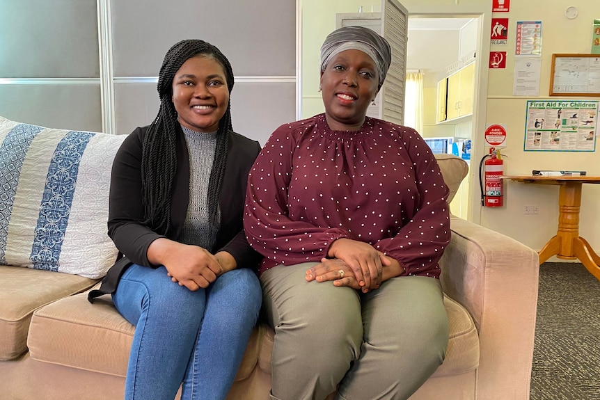 Two smiling women sitting side by side on a sofa indoors