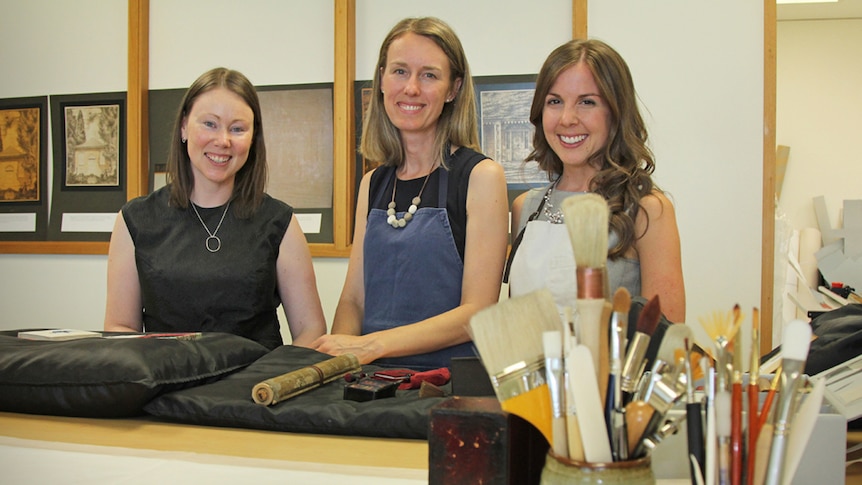 Three girls pictured next to historical books and objects.