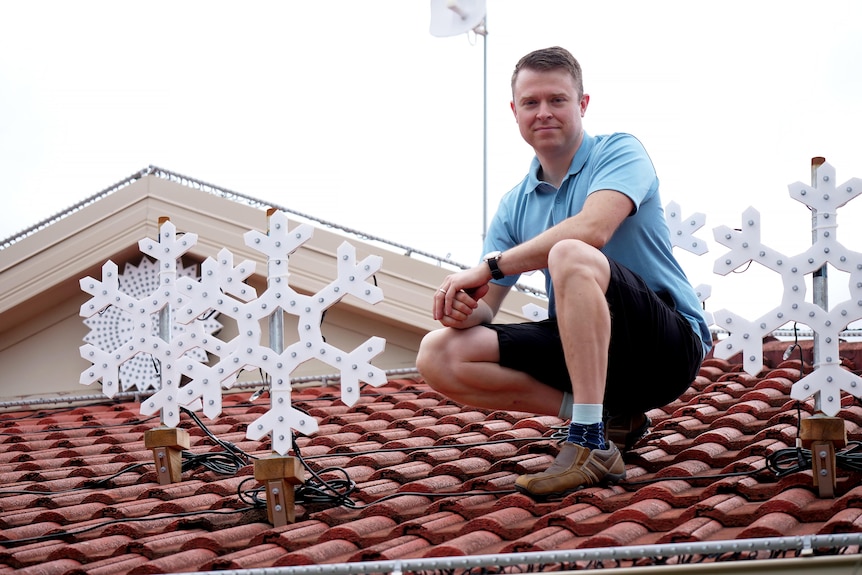 Nick Triantafillou est assis sur son toit, à côté de quelques lumières de Noël blanches en forme de flocon de neige.