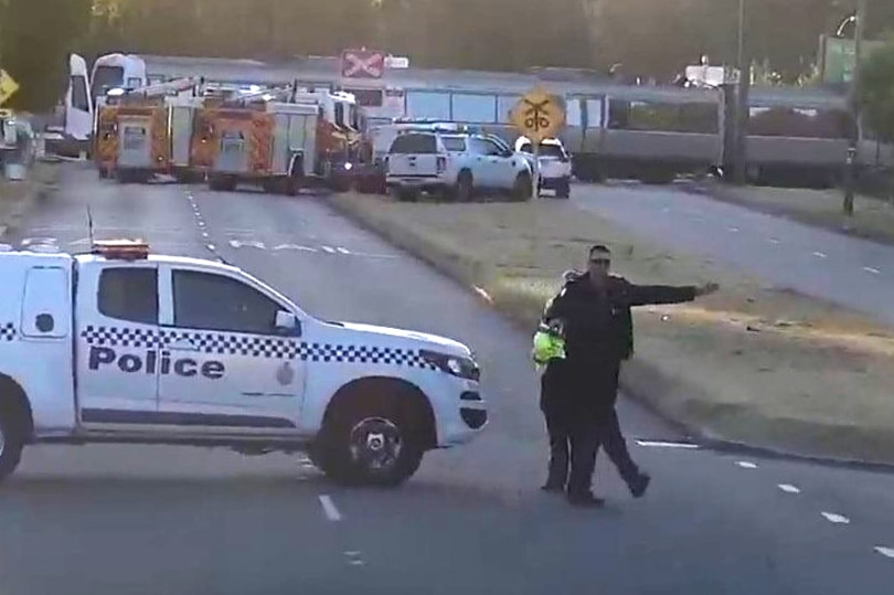 A police car parked across the road with an officer int he foreground and a train in the rear.