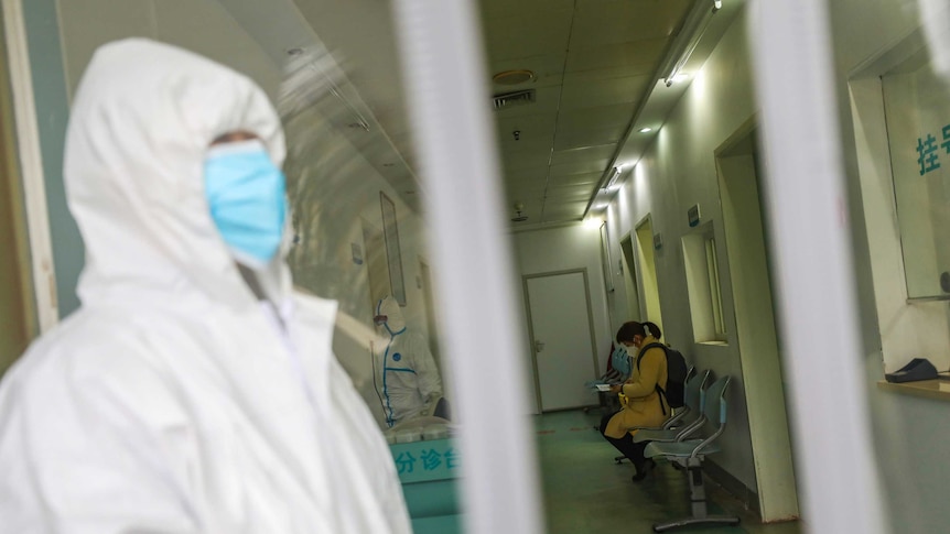 Medical workers in protective gear stand as a woman suspected of being ill with coronavirus waits in Wuhan.