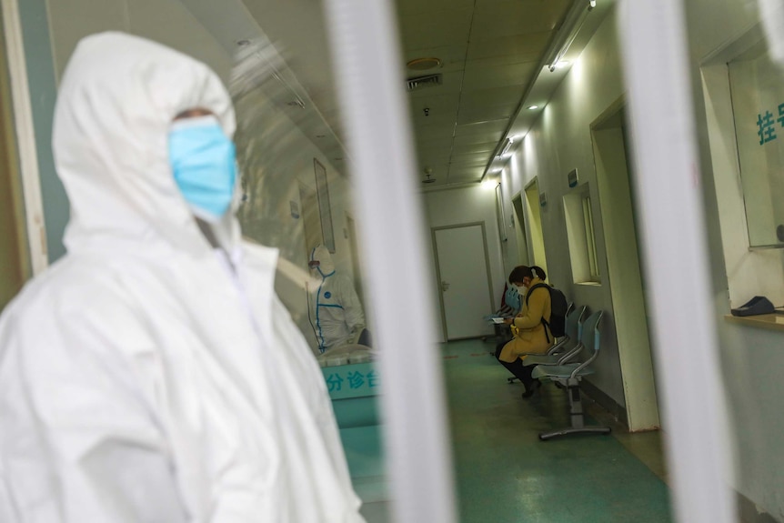 Medical workers in protective gear stand as a woman suspected of being ill with coronavirus waits in Wuhan.