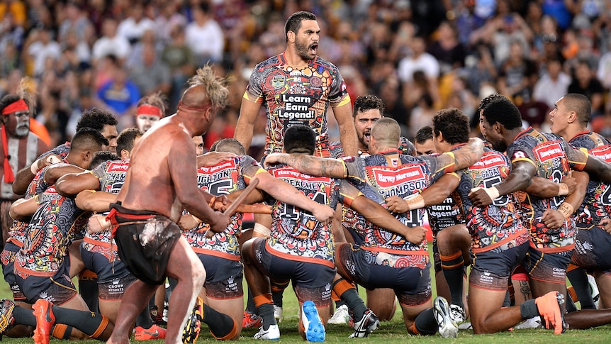 Man standing in the middle of a group huddle while performing a cultural war cry 