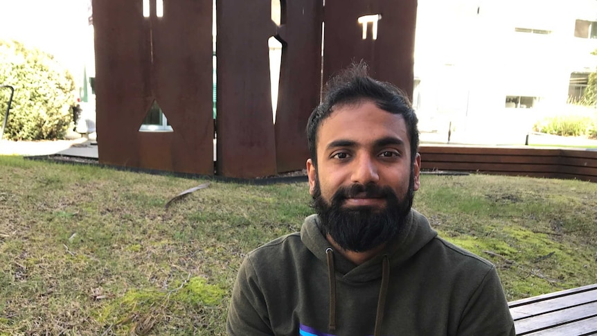 Microbiologist Dipon Sarkar sits in front of a pi sign at the UTAS campus in Sandy Bay