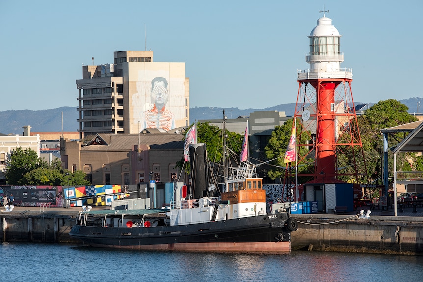 A brightly coloured lighthouse stands nearby a steamer and apartment decorated with a mural 
