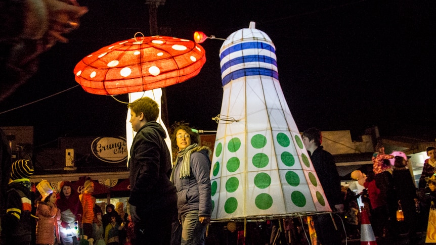 Lanterns in the shape of a mushroom and a Dalek in a night time street parade.