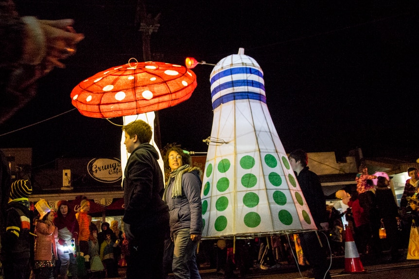 Lanterns in the shape of a mushroom and a Dalek in a night time street parade.