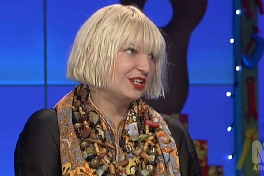 A woman with a blonde bob speaks during the filming of a television show.
