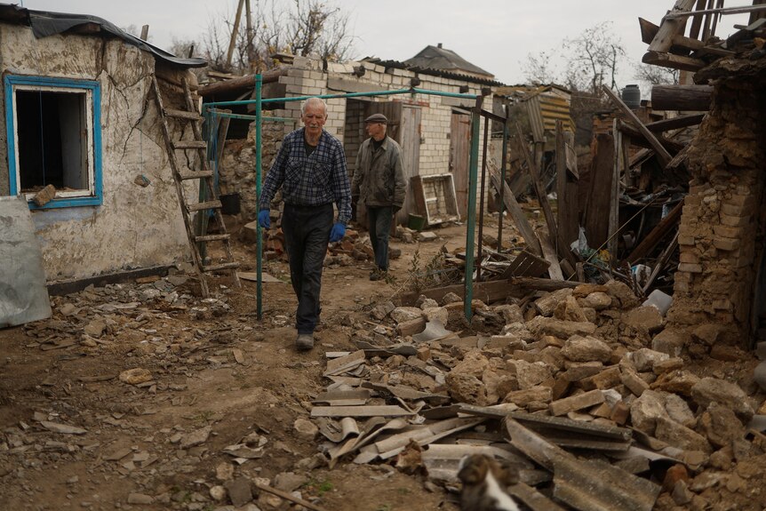Two elderly men walk past destroyed homes.