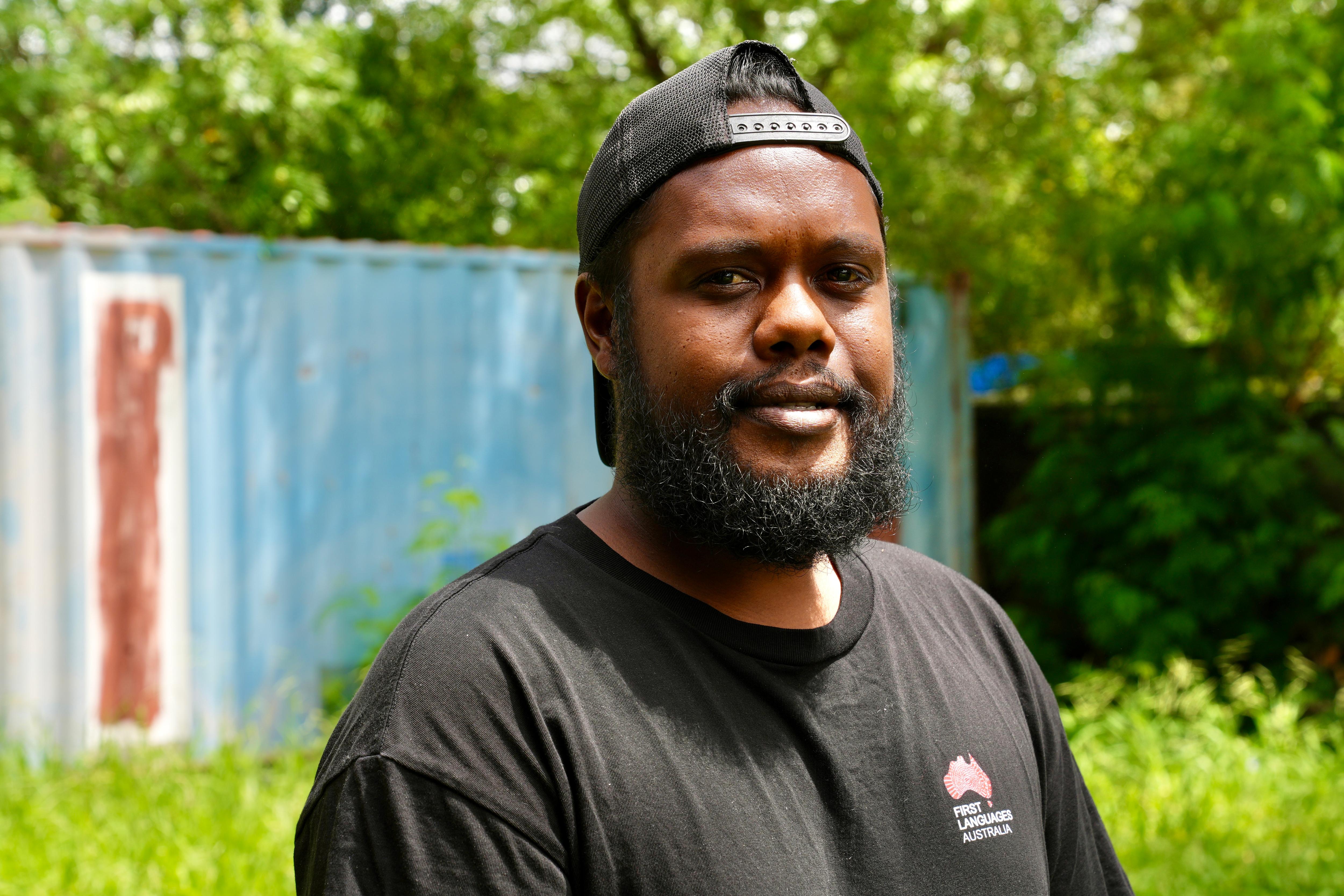 Joven aborigen con barba negra y sombrero en un jardín. 