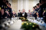 Vladimir Putin holding a champagne flute aloft in front of a table lined with standing Russian soldiers