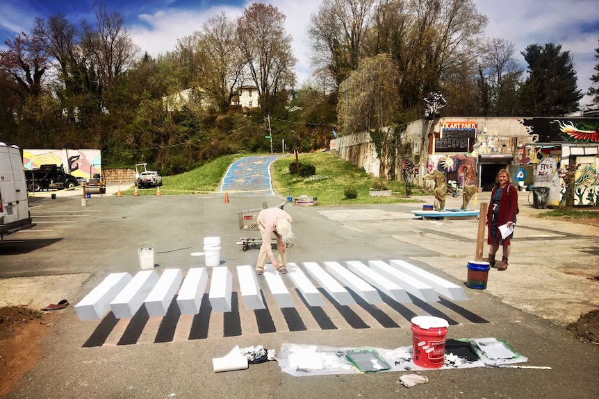 A woman watches as someone paints an optical illusion three dimensional zebra crossing on the road in the United States