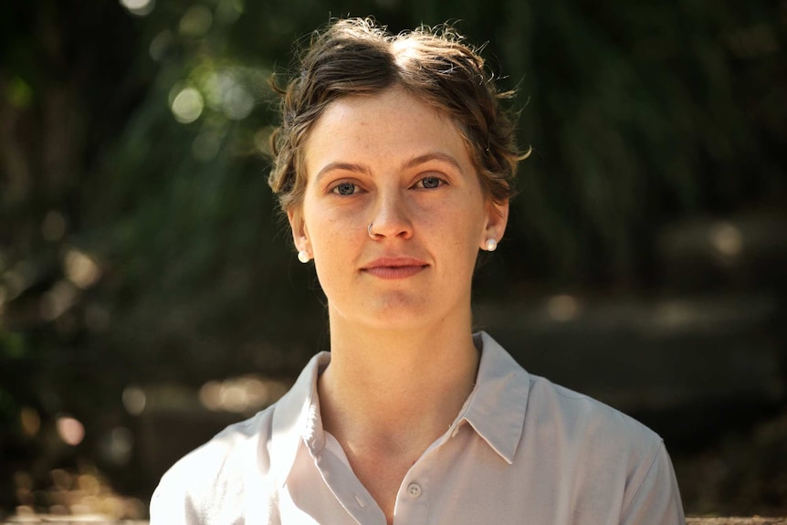 Head shot of Mel McAuliffe standing outside with out of focus trees in the background.