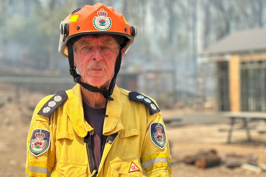 A man in an yellow firefighting jacket and orange hard hat looks at the camera.