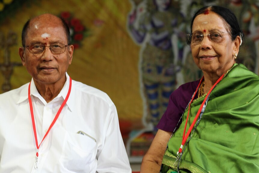 An elderly Indian couple sit facing the camera