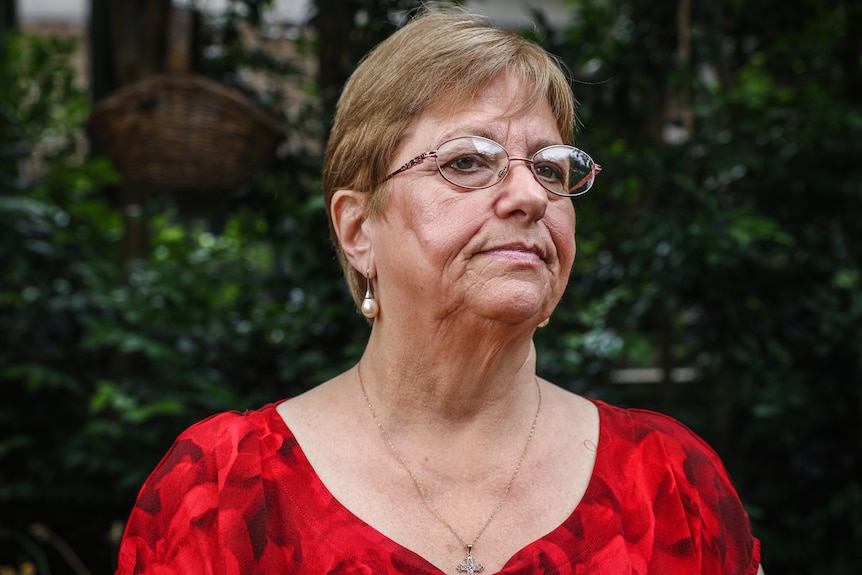 A woman in glasses and a red top looks solemnly to her left