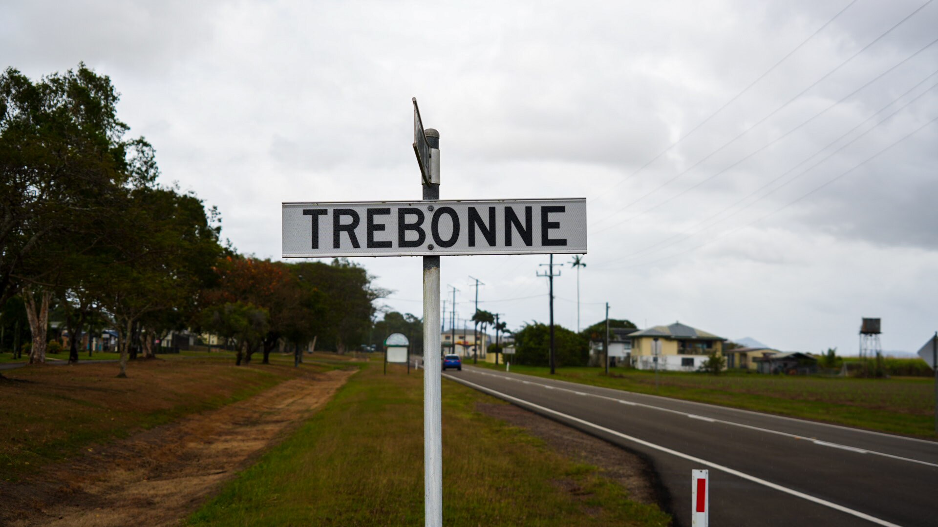 White street sign with Trebonne in black lettering. Road and trees behind it.