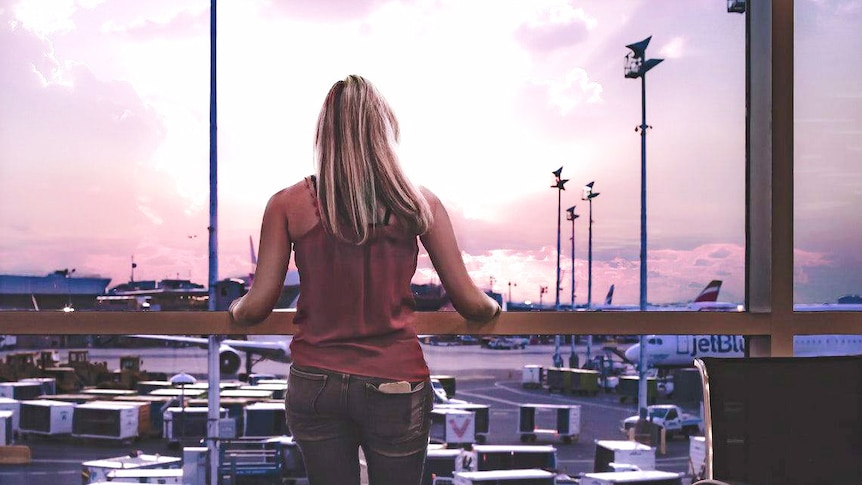 Woman stands at airport window looking at planes to depict travellers' tips for having a better flight.